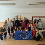 Young Erasmus+ participants from EVEC Athens and partner organisations holding the EU flag at the June 2026 youth project in Spain