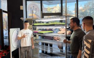 Participants stand beside a microgreens growing rack with lit trays during an EVEC training course in Athens