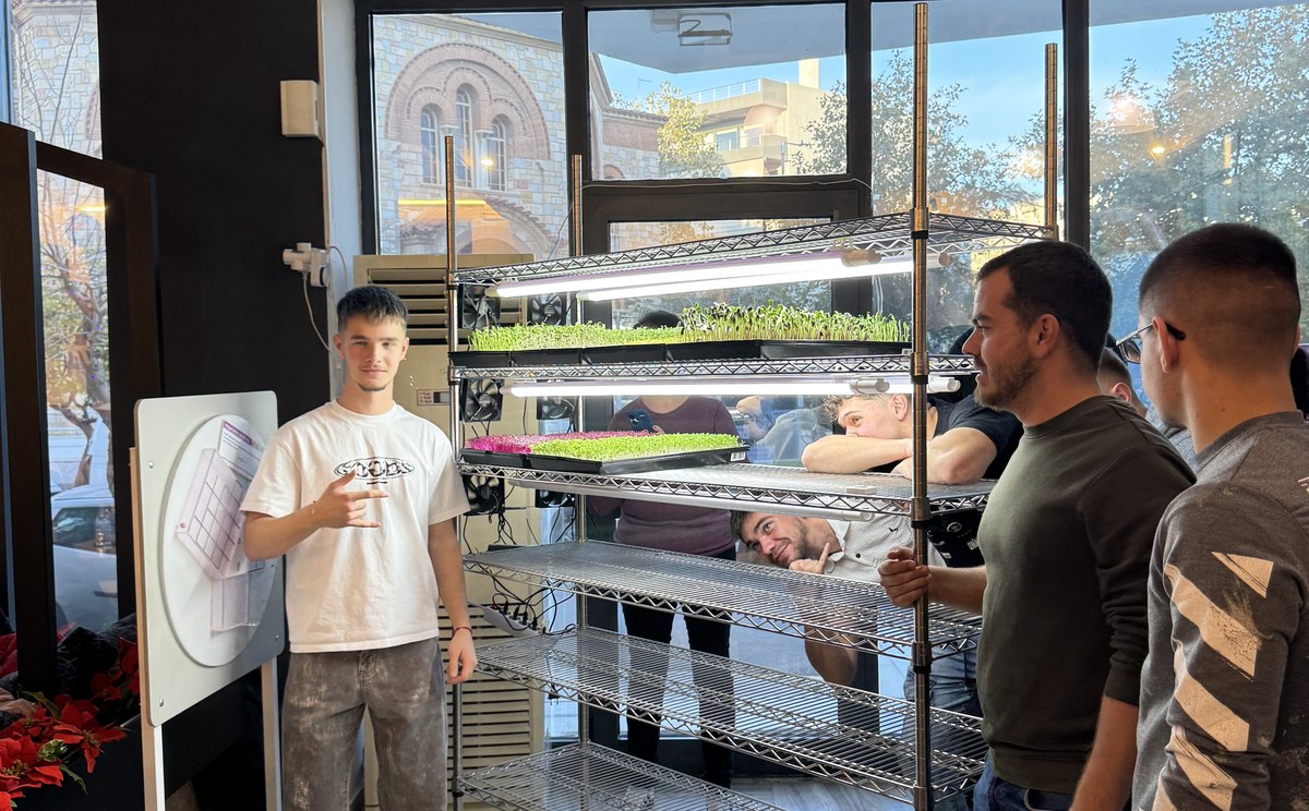 Participants stand beside a microgreens growing rack with lit trays during an EVEC training course in Athens