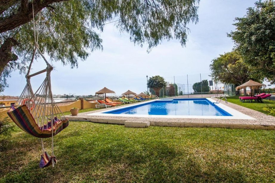 Garden of Cortijo Amaya with a hammock, a lawn and the swimming pool under a blue sky